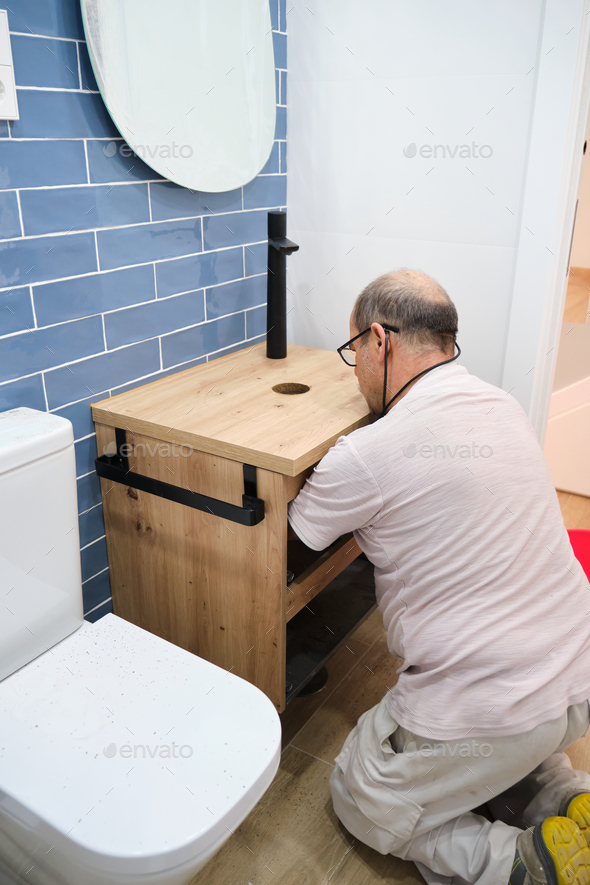 Senior plumber installer installing sink drain tube. Stock Photo by